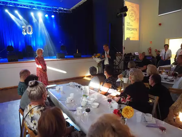 Wójt składa życzenia seniorom, przekazując kwiaty dyrektor GBPiCK