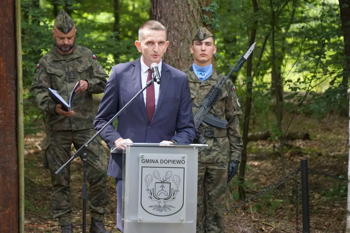 Wójt Sławomir Skrzypczak przy mównicy w lesie. Za nim wojskowi