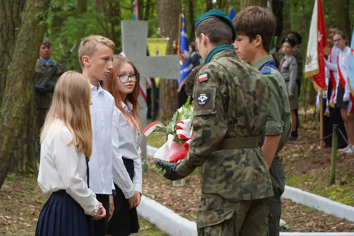 Uczniowie przekazują wiązankę kwiatów harcerzom